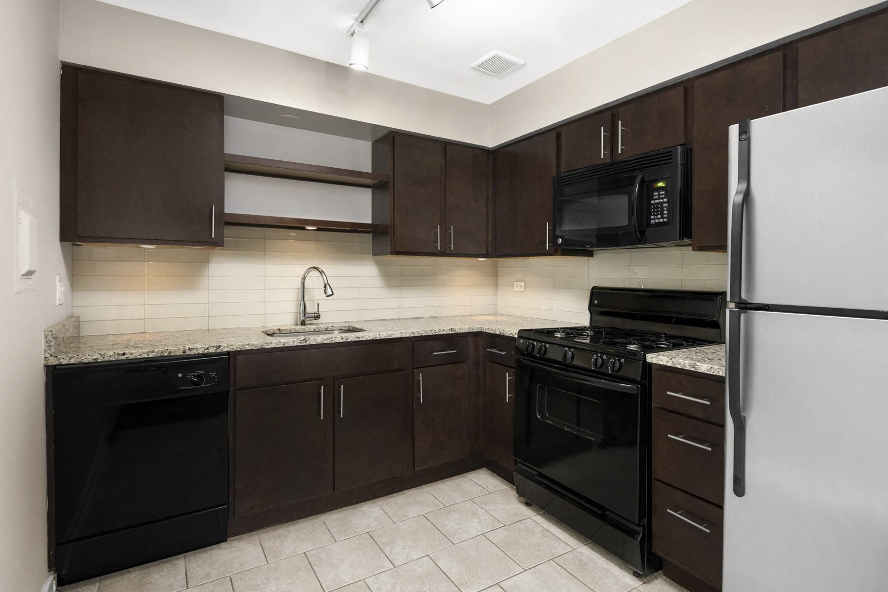 Modern kitchen with dark wood cabinets, granite countertops, and stainless steel appliances.