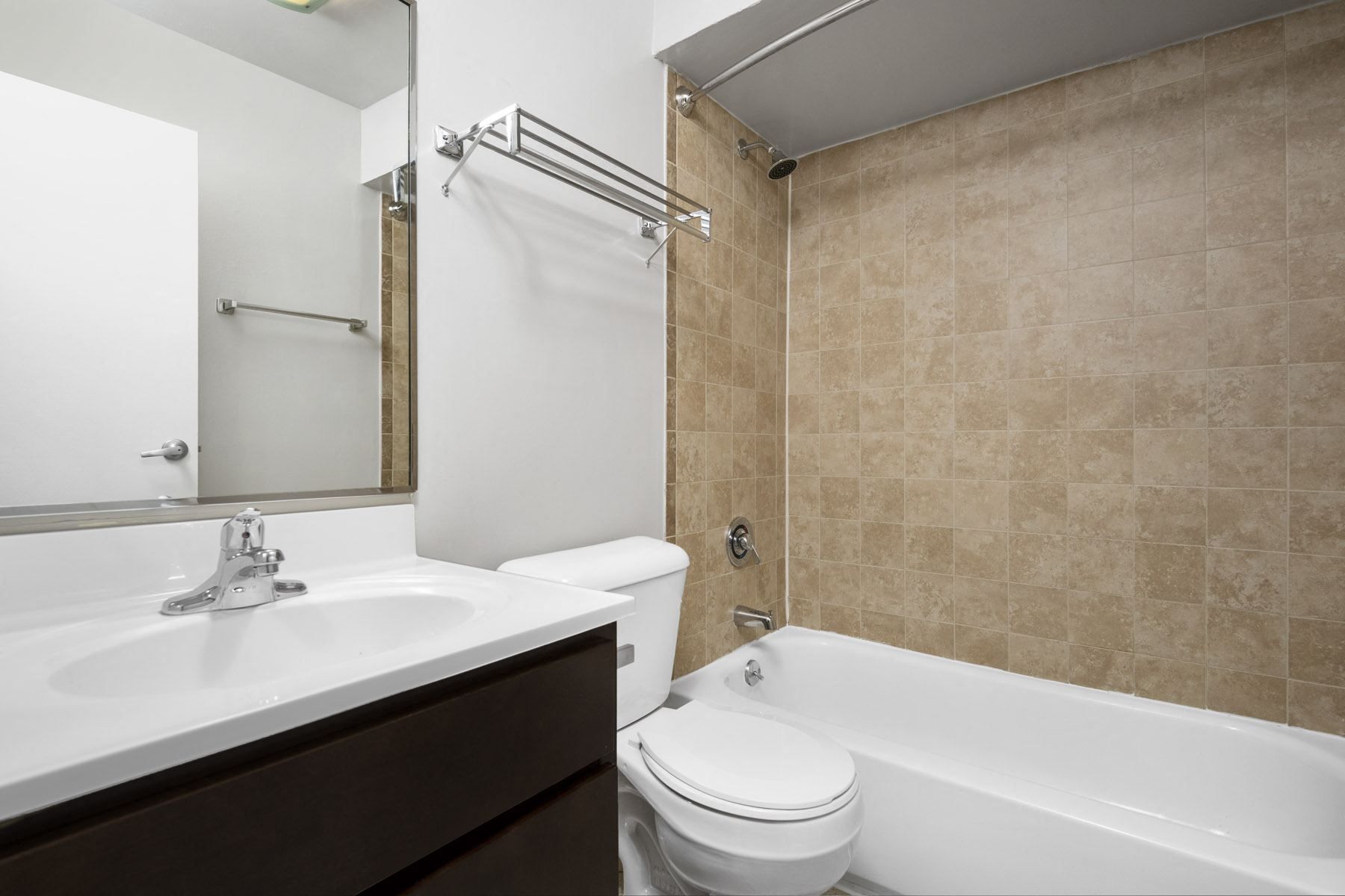 Bathroom vanity with sink and mirror, toilet, and bathtub with tiled shower wall.