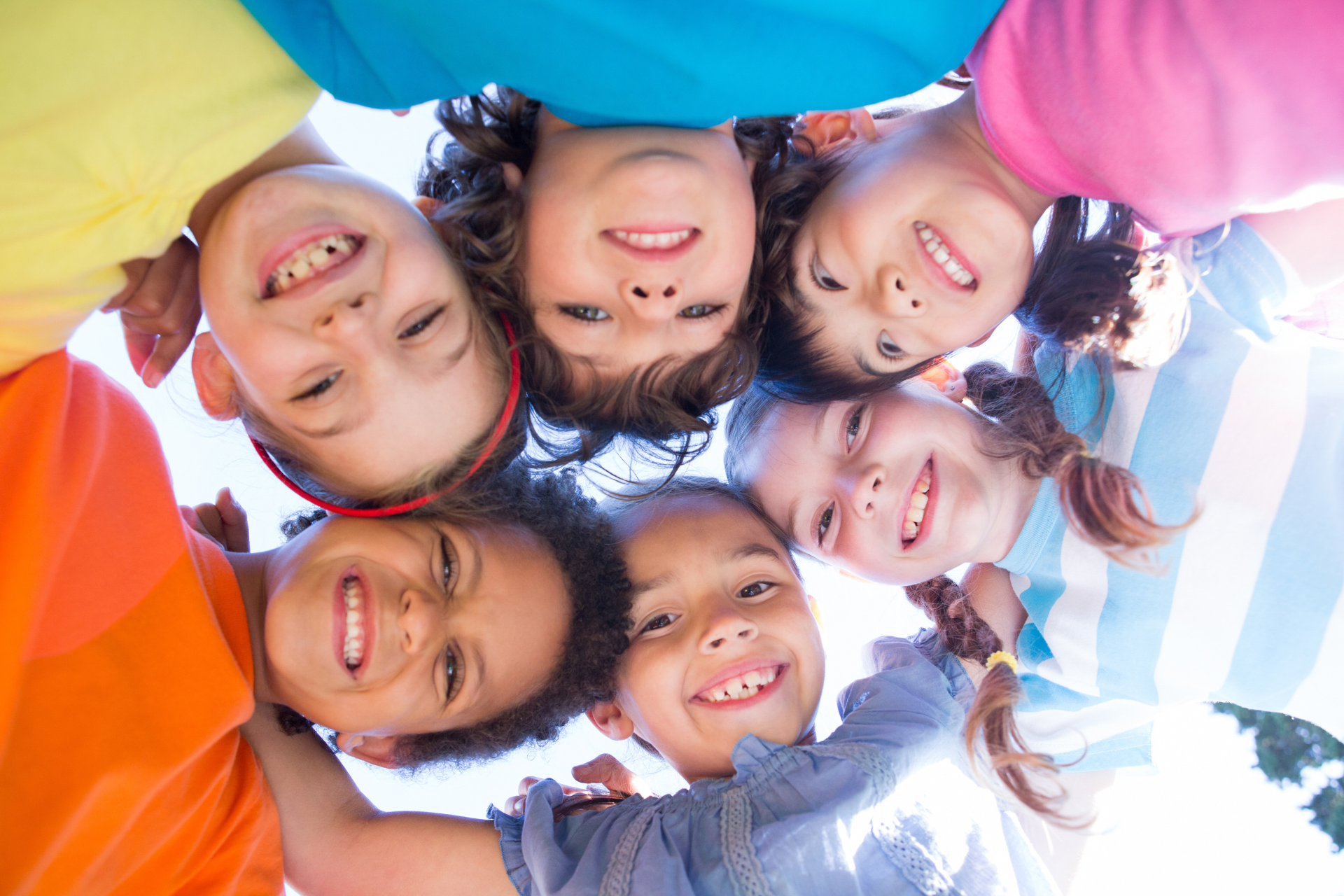 Eine Gruppe lächelnder Kinder in bunten Hemden blickt aus einem niedrigen Winkel nach unten.