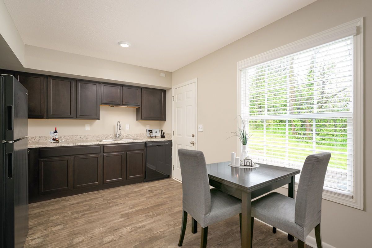 Kitchen with dark wood cabinets and appliances, light wood flooring, and a small dining table with two grey chairs.
