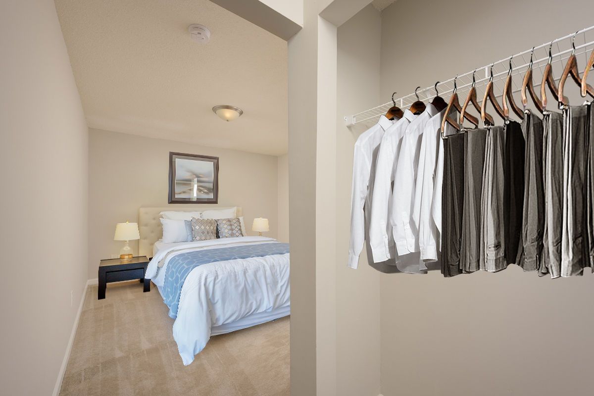 A view into a bedroom from a walk-in closet featuring white shirts and dark trousers on a hanging rack.