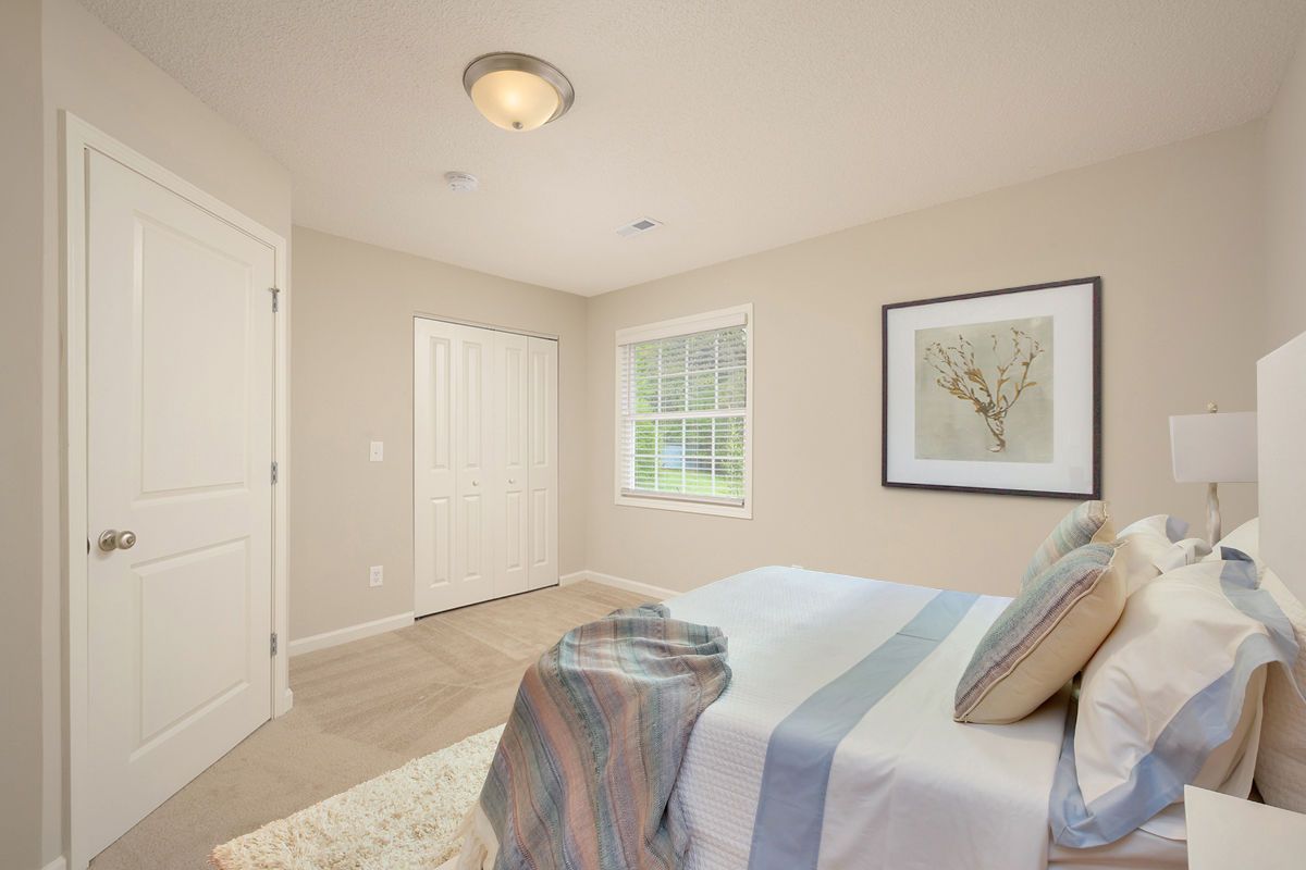 A light-colored, minimalist bedroom featuring a bed with blue and white bedding, a window, and a closet with white doors.