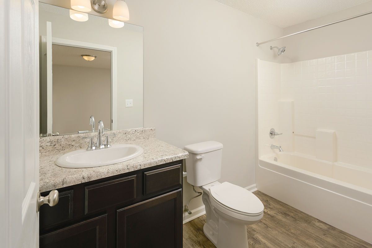 A clean bathroom with a dark wood vanity, speckled stone countertop, white toilet, and a shower-tub combo.