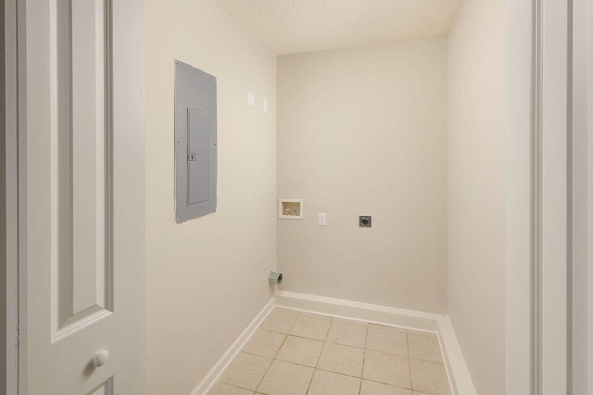 Empty laundry closet with neutral walls, tiled floor, a circuit breaker panel, and water hookups for a washer and dryer.
