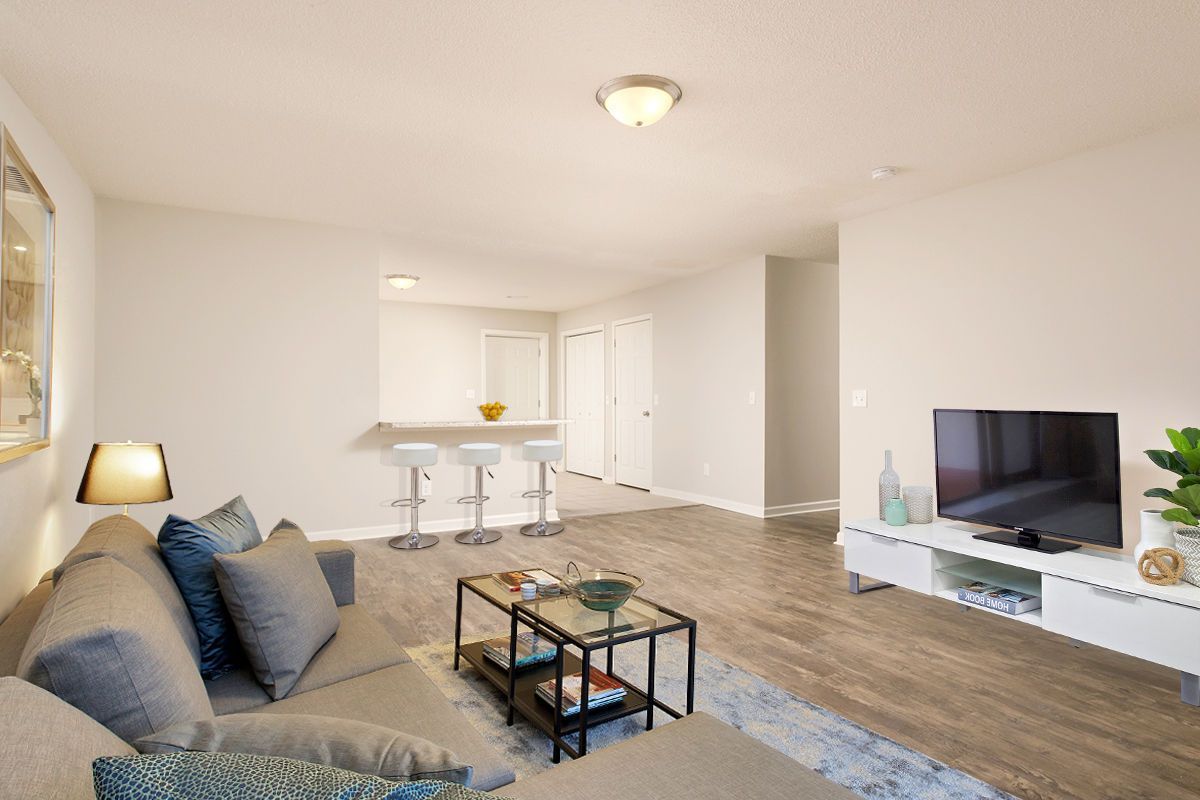A modern living room with a grey sofa, coffee table, white media console with a TV, and a bar area with three stools.