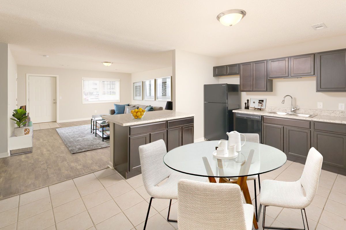 An open-plan apartment featuring a kitchen with dark cabinetry, a glass dining table, and a living area with a rug.