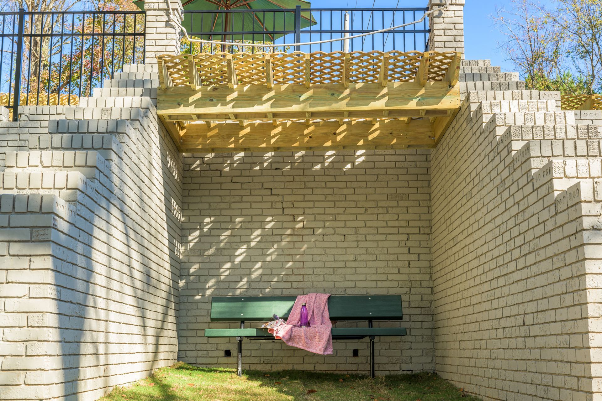 A green bench sits beneath a wooden deck, set into a recessed area between two white brick retaining walls.