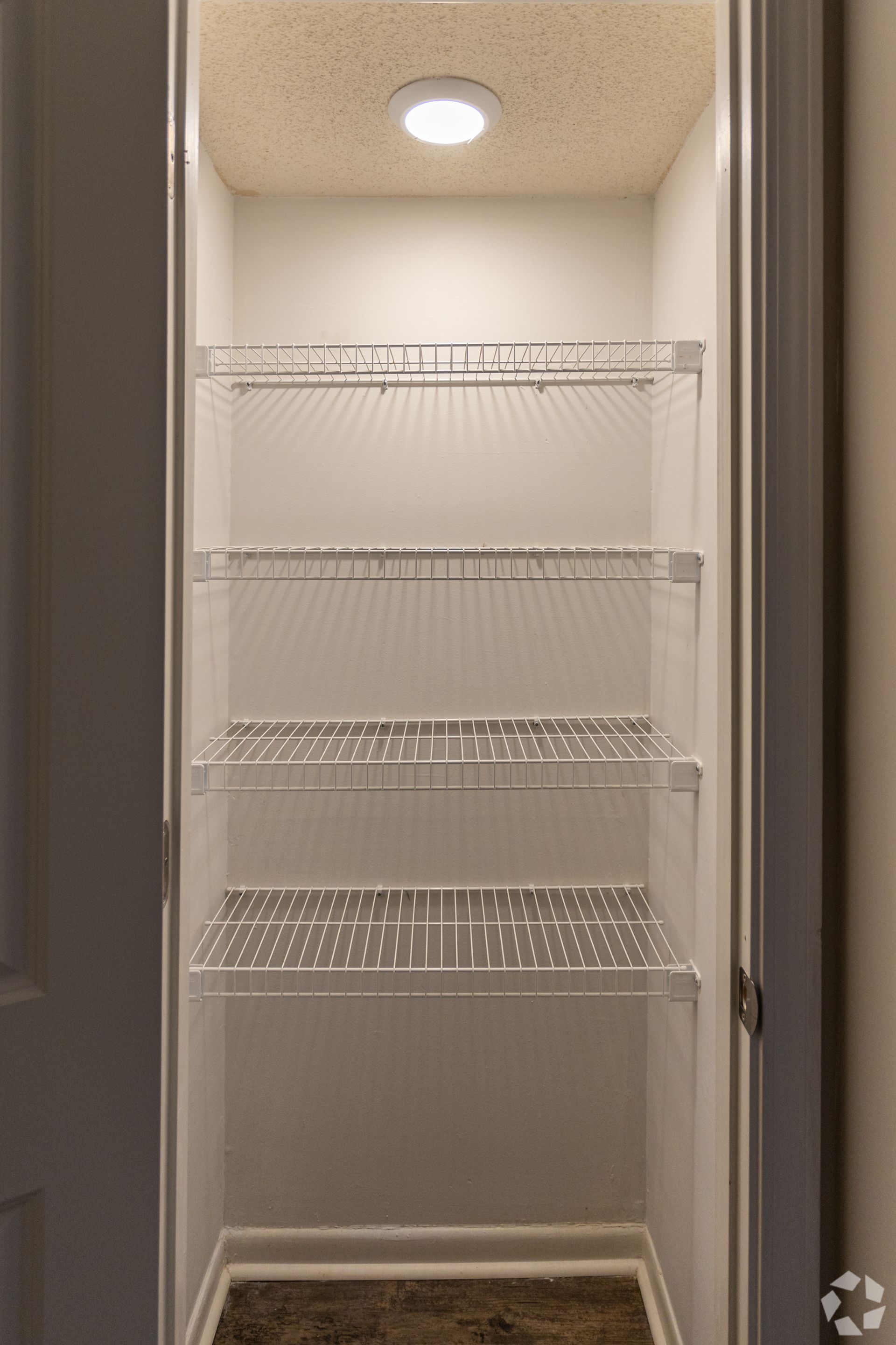 A white reach-in closet with wire shelving and a circular overhead light against a textured ceiling.