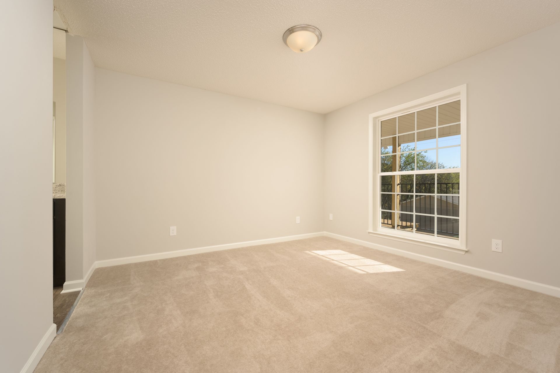 Empty room with light gray walls, neutral carpeting, a central ceiling light, and a window with white trim.