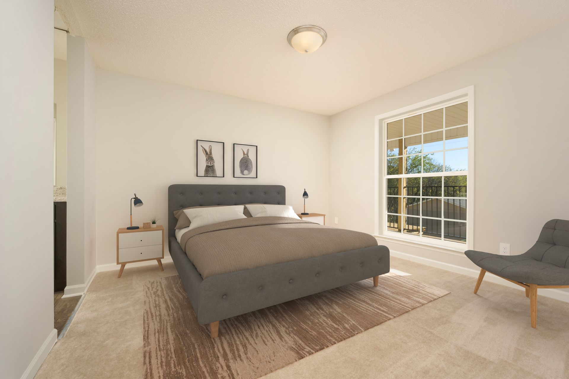 A bedroom with a gray tufted bed, beige area rug, two framed wall prints, a nightstand, and a gray accent chair.