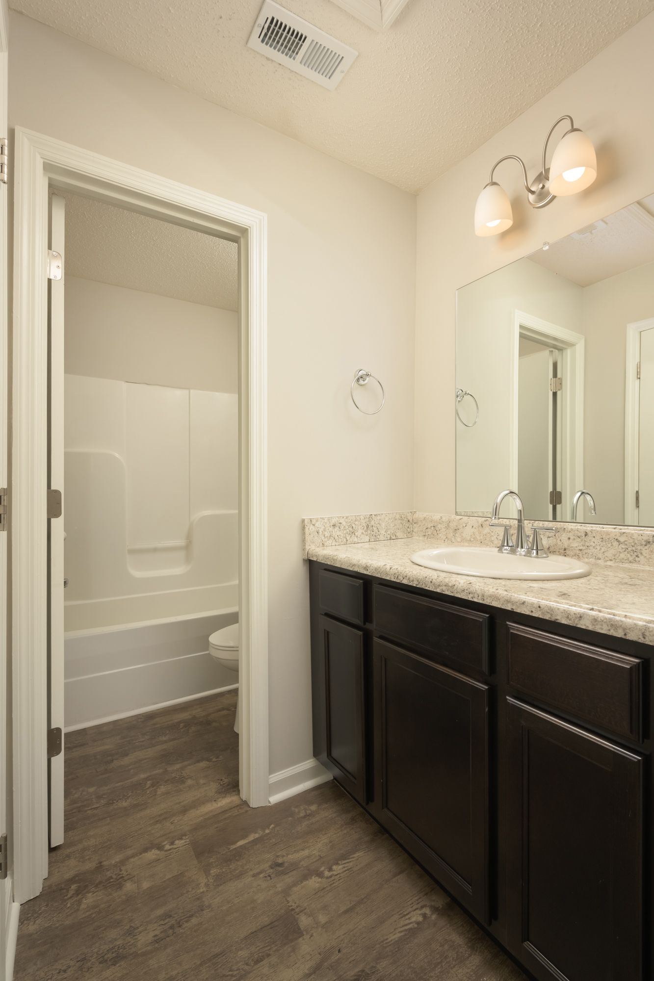 A modern bathroom featuring a white vanity with speckled countertops, dark cabinets, a mirror, and a connected tub shower.