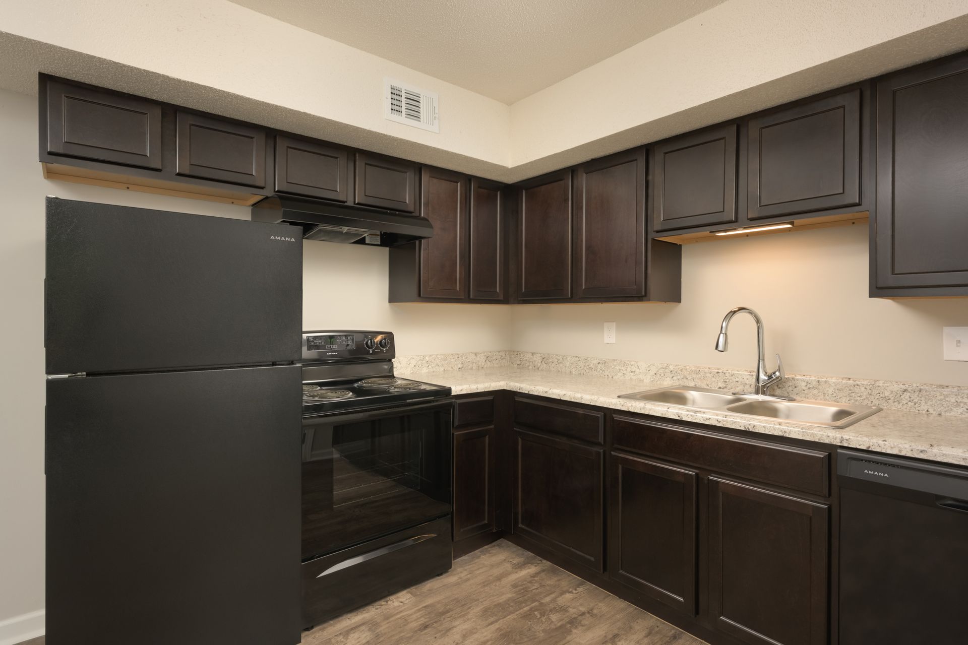 A kitchen with dark brown cabinets, a black refrigerator, a black oven range, and light-colored countertops.