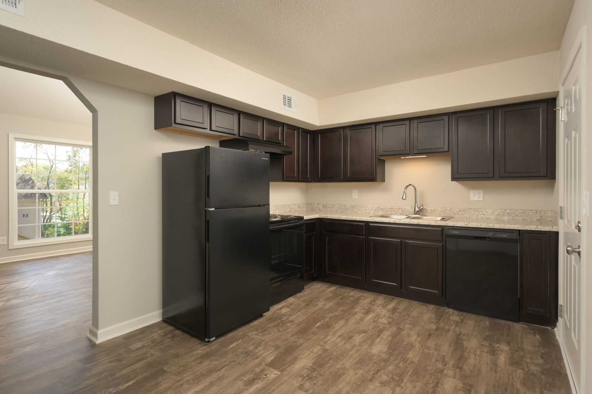 A modern kitchen with dark brown cabinets, black appliances, light beige walls, and light brown wood-look flooring.