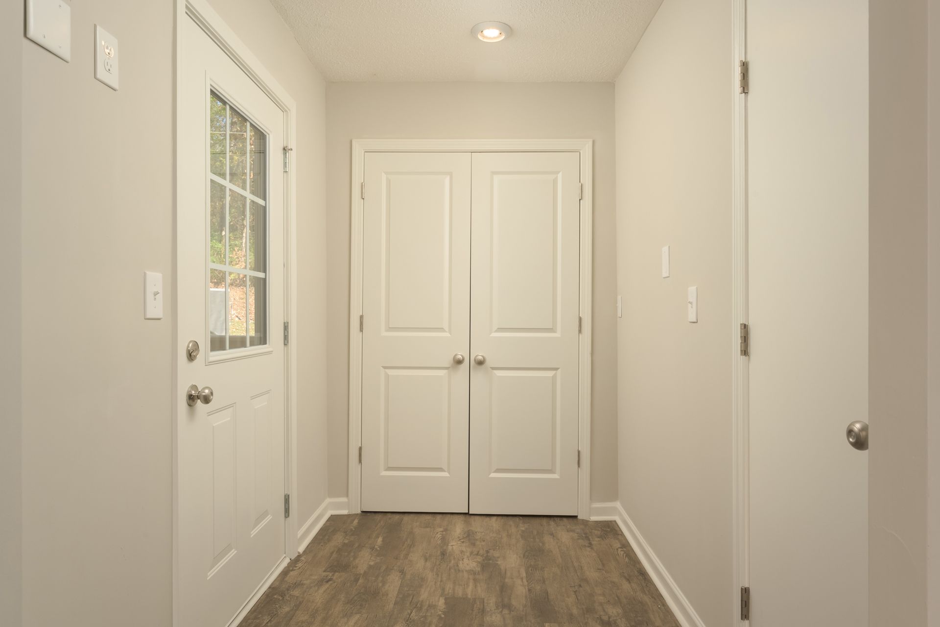 An interior entryway with light walls, wood-look flooring, a front door with a window, a double-door closet, and one door.