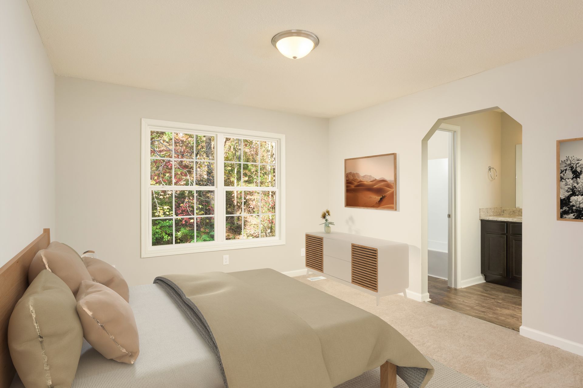 A bright bedroom featuring a queen bed with beige bedding, a dresser, and an arched doorway leading to a bathroom.