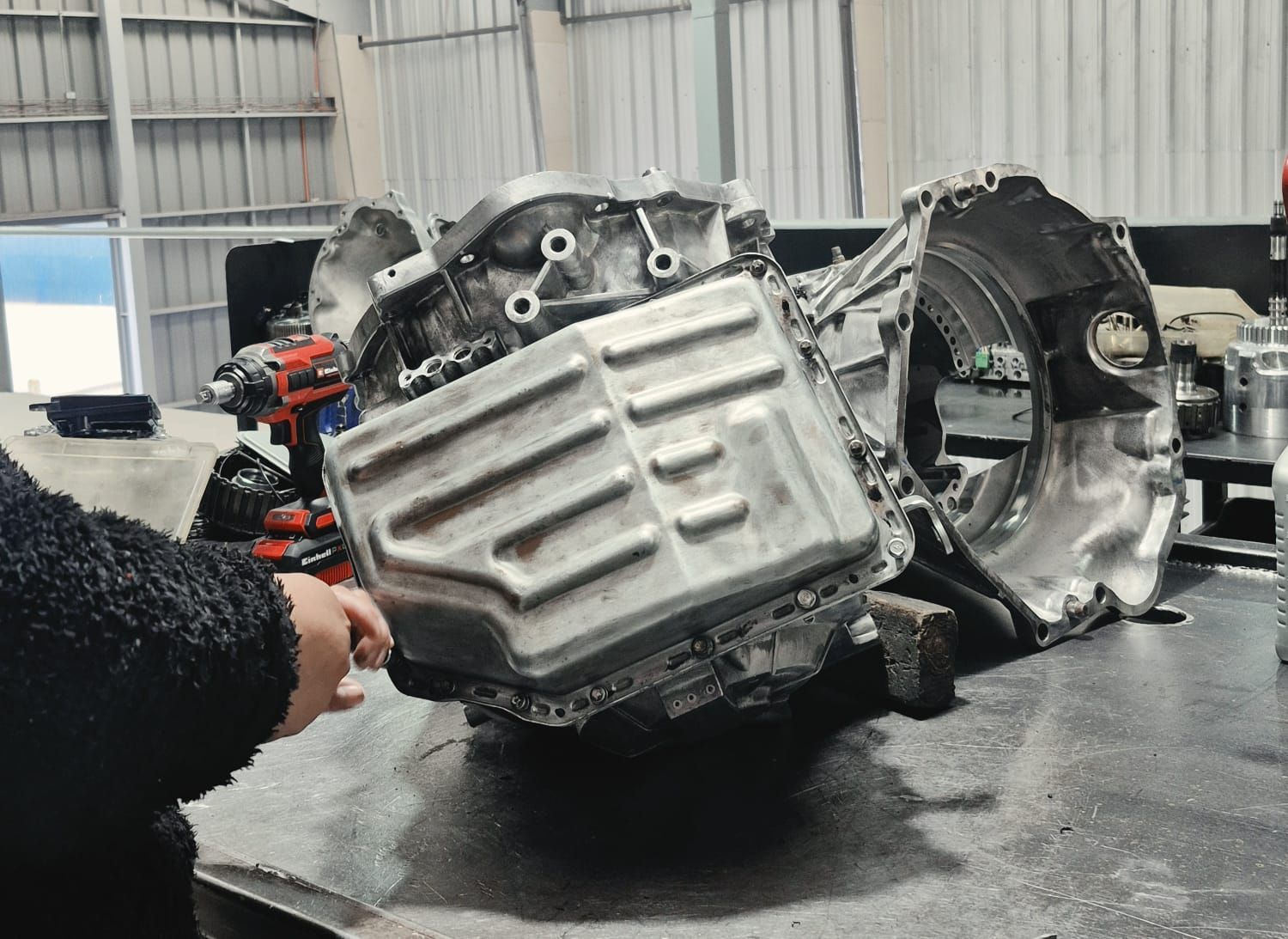 Mecánico con mono azul trabajando bajo el capó de un coche en un taller de reparación de automóviles.