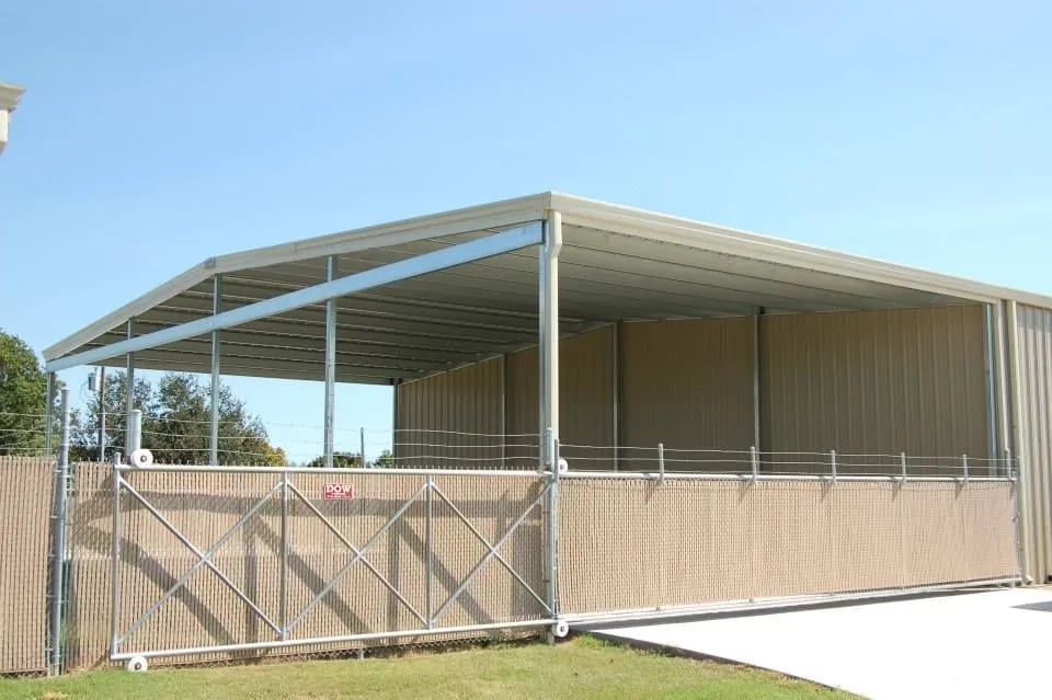 Metal shed with tan walls, open front, on a grassy area, blue sky.