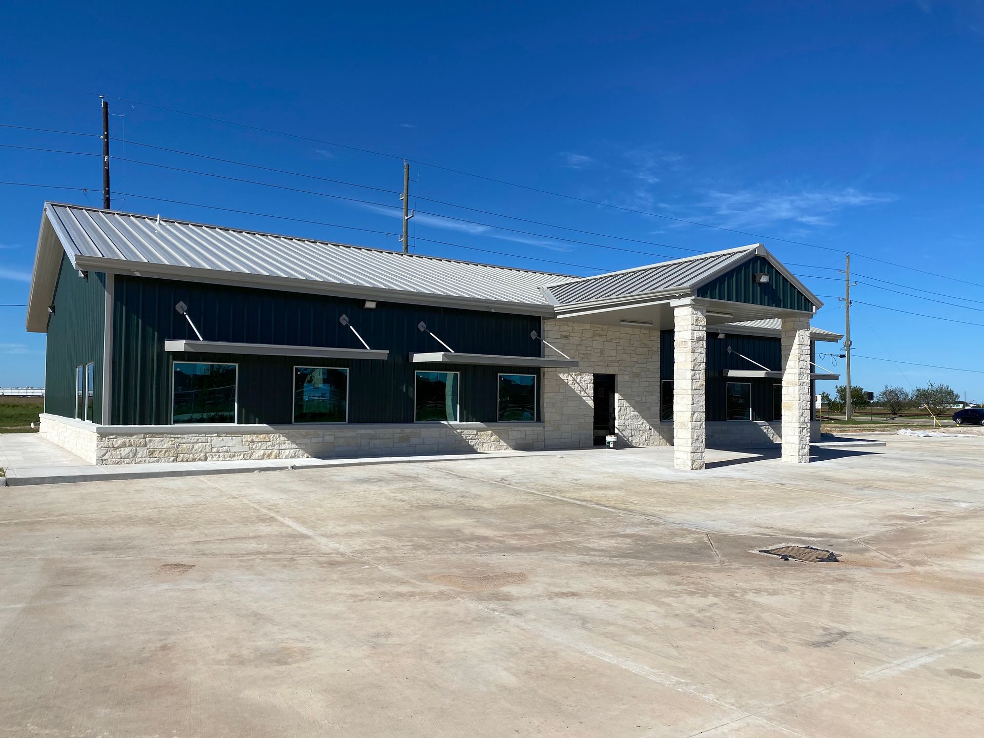 Green and gray commercial building with stone accents under a clear blue sky.