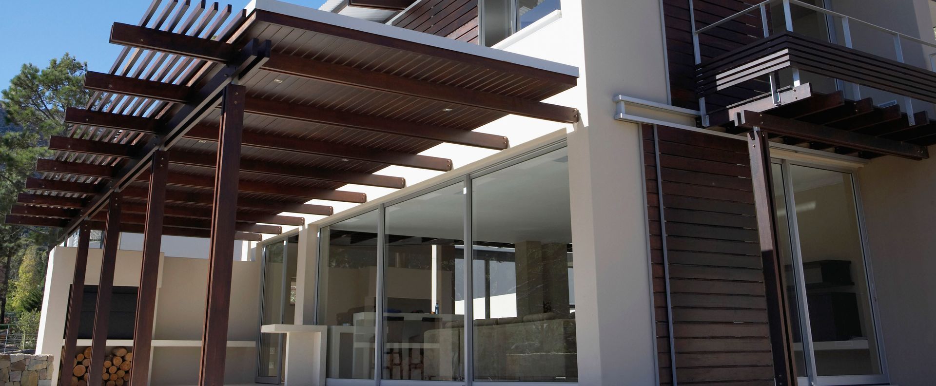 Wooden pergola over a building with glass doors and windows.