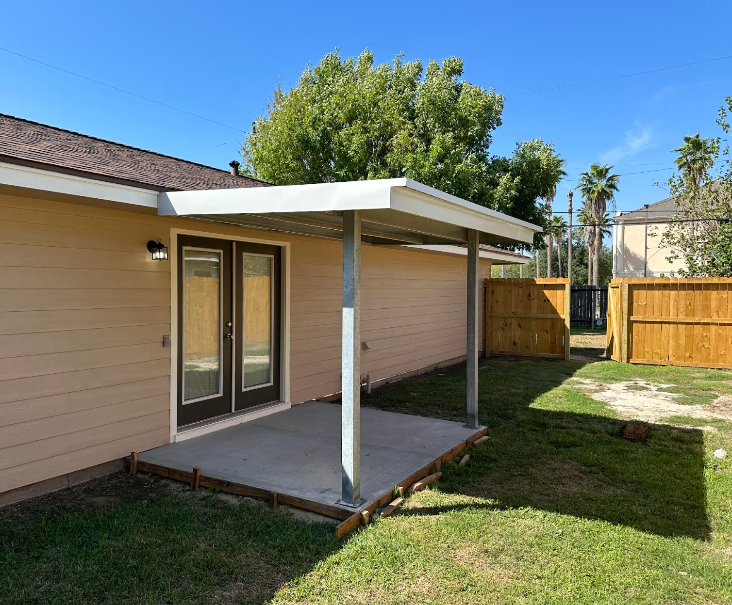 Metal-sided shed with open center area. Beige walls, blue trim. Trees and grassy area in background.