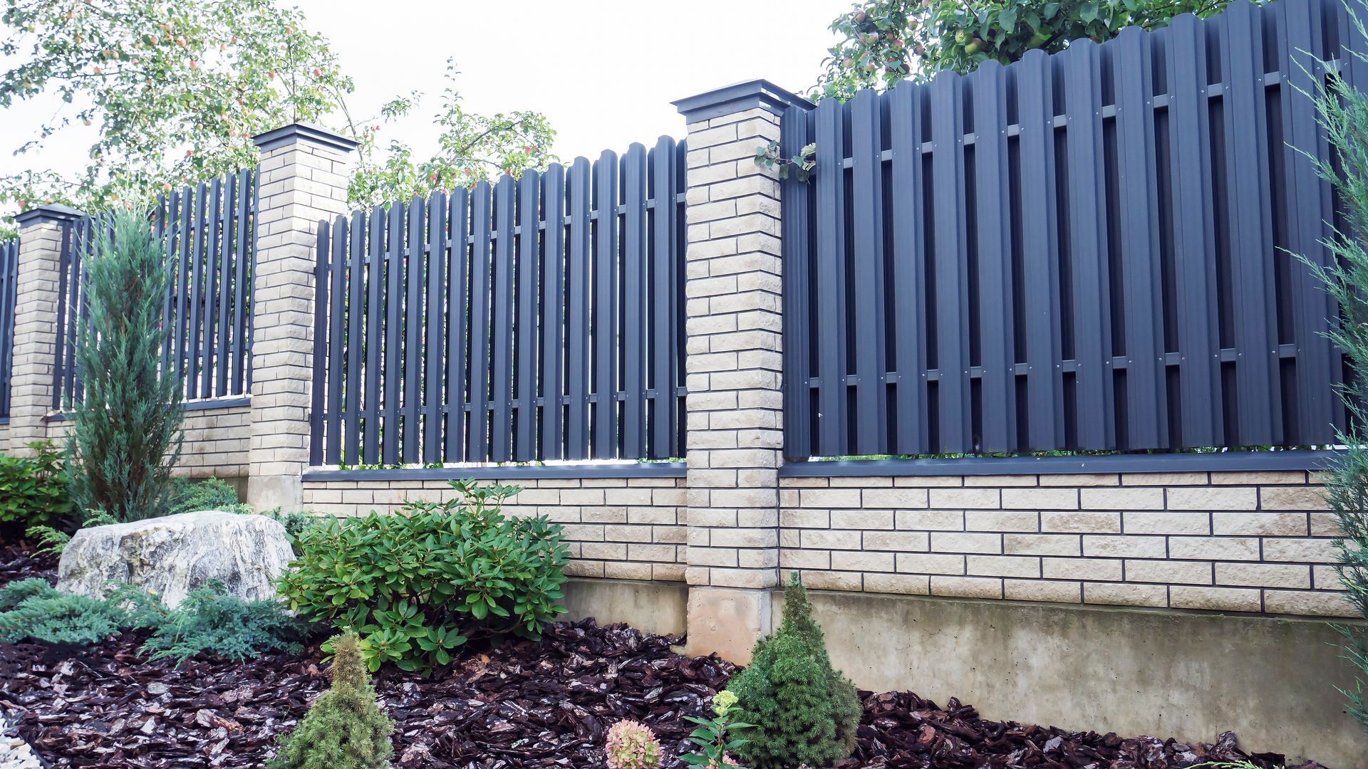 A black fence is surrounded by brick pillars in a garden.