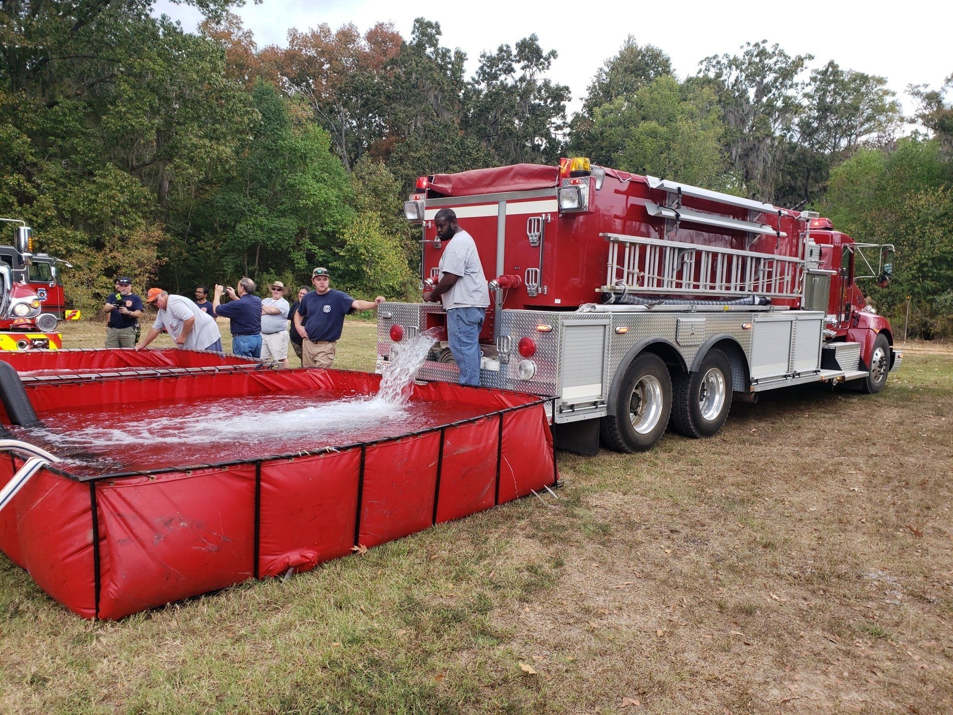 A fire truck is pouring water into a red tank.