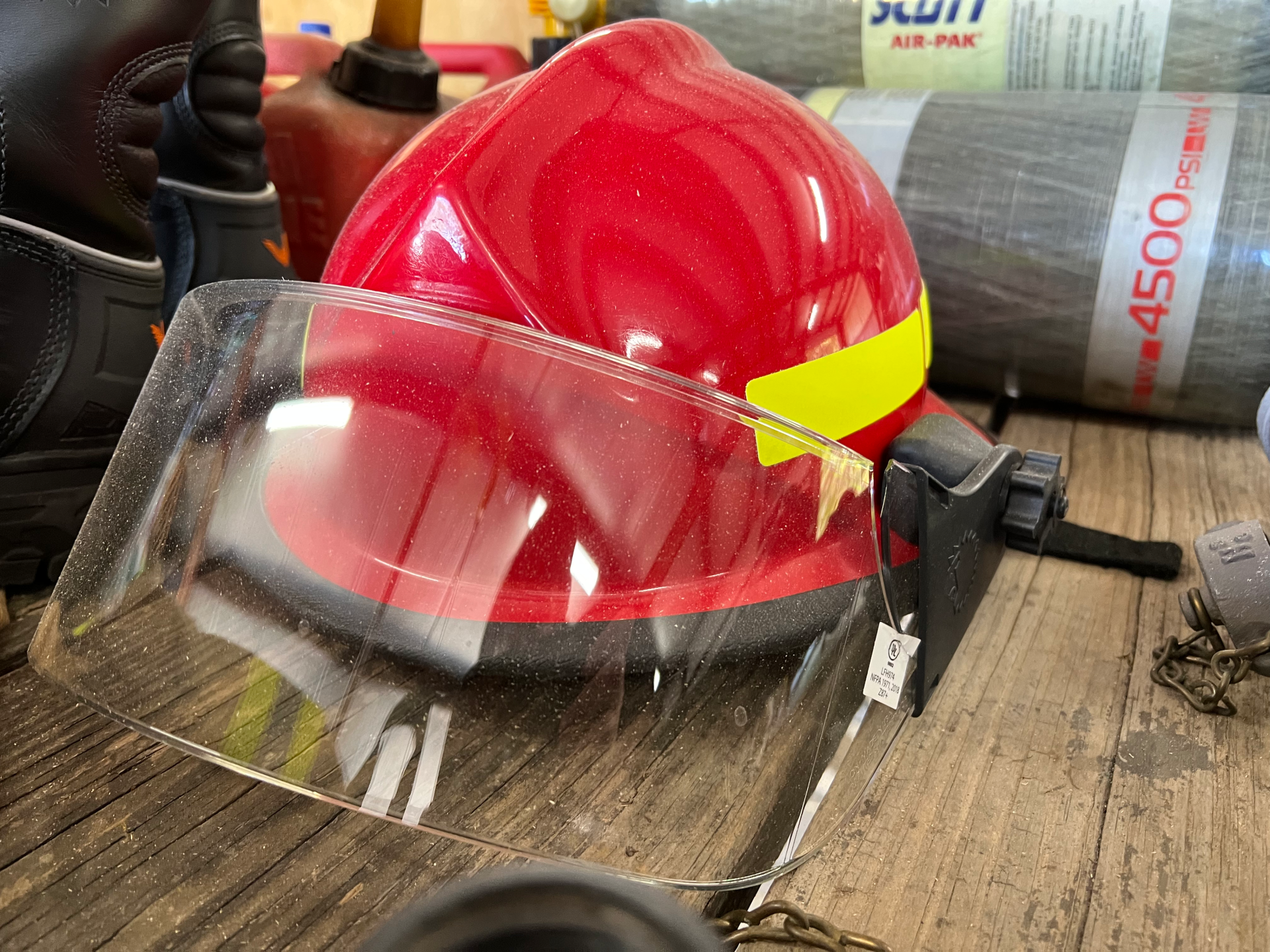 A red fire helmet with a yellow stripe is sitting on a wooden table.