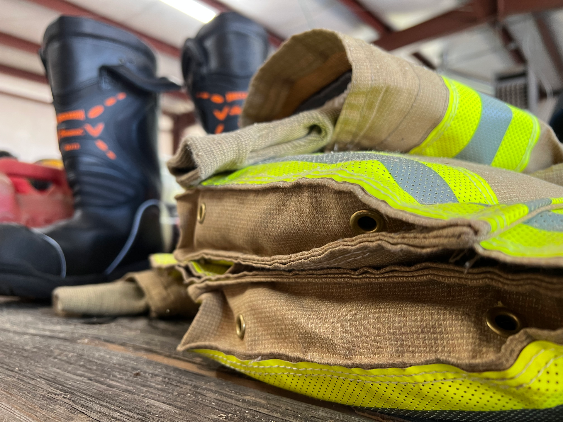 A stack of firefighter gloves and boots on a wooden table.