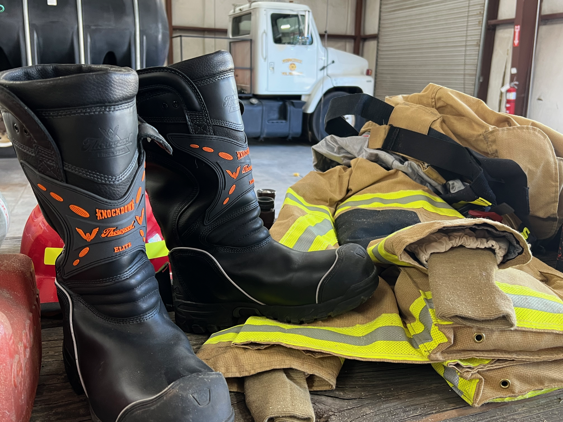A pair of firefighter boots are sitting on top of a pile of fire fighting gear.