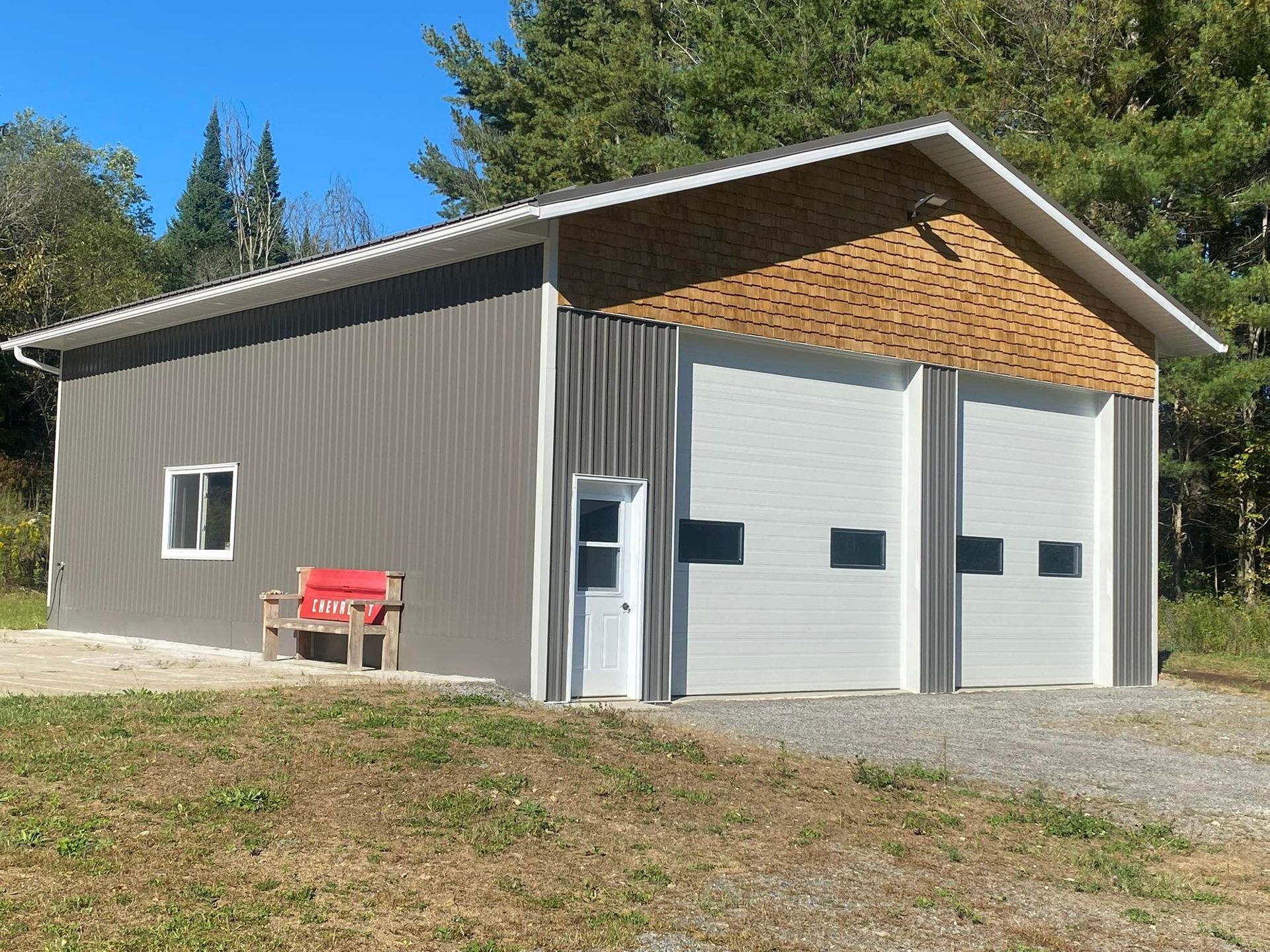 Gray garage with two white doors and red bench beside it on a sunny rural lot | Penner Auto