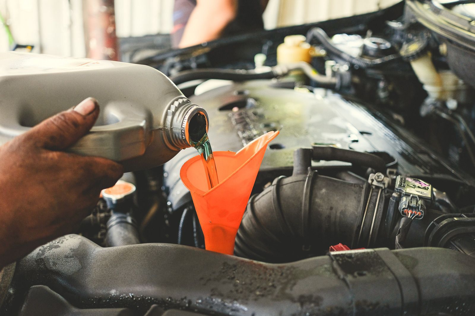 Hand pouring coolant into a car engine through a bright orange funnel