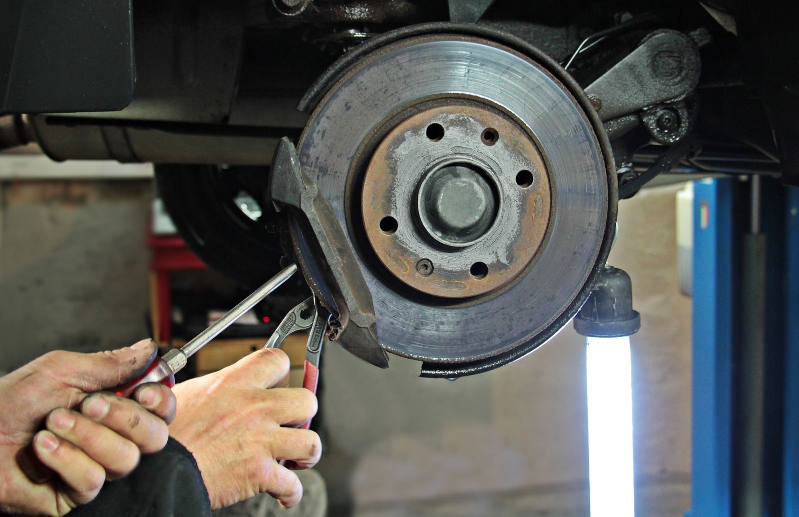 Mechanic repairing a car brake rotor with tools in a garage lift area
