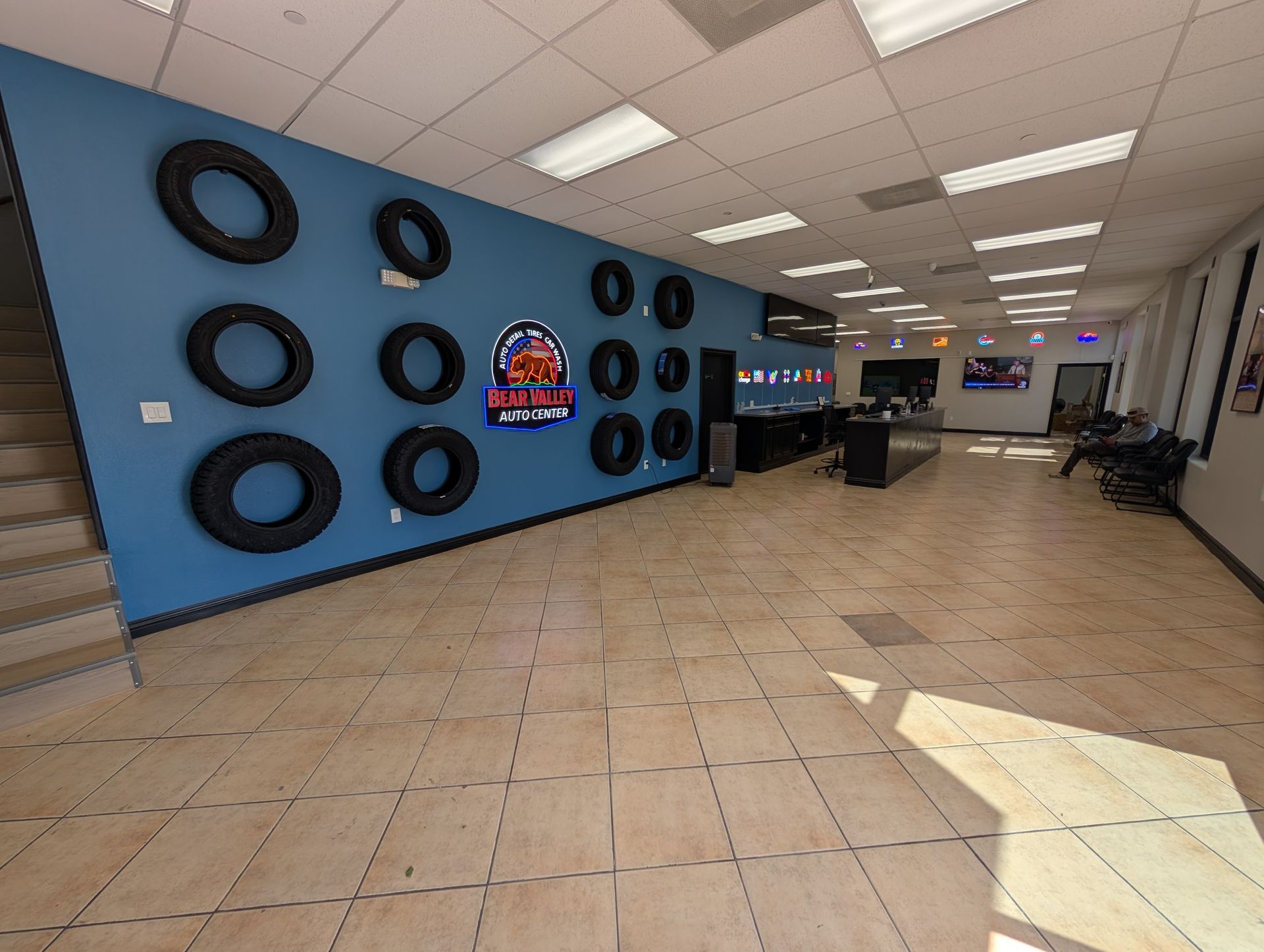Auto shop lobby with blue tire wall art, tiled floor, desks, and chairs under bright ceiling lights