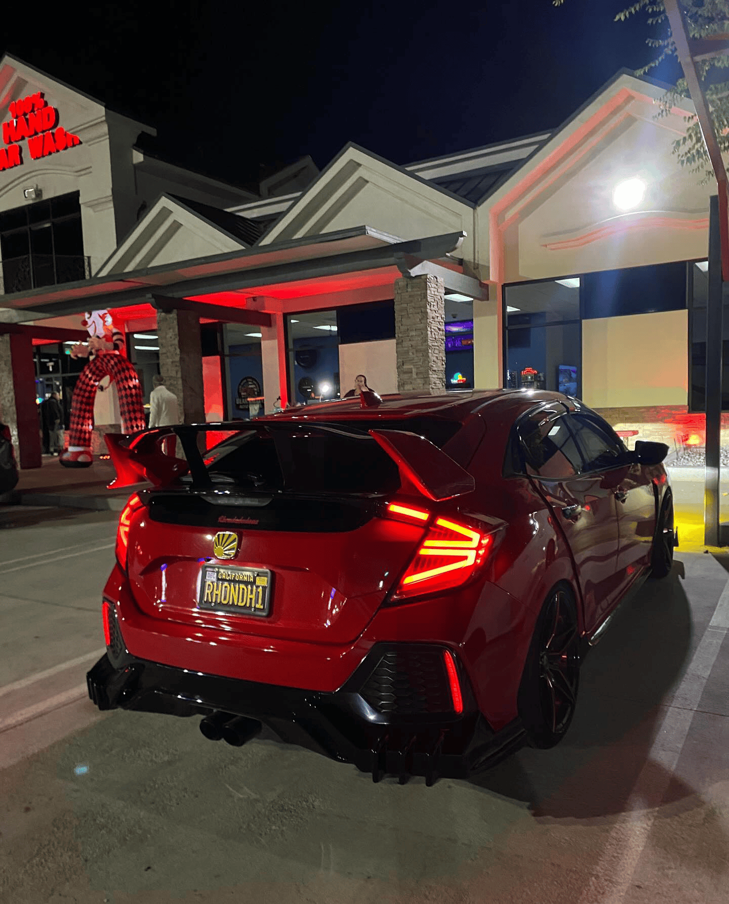 Red hatchback parked at a brightly lit restaurant entrance at night