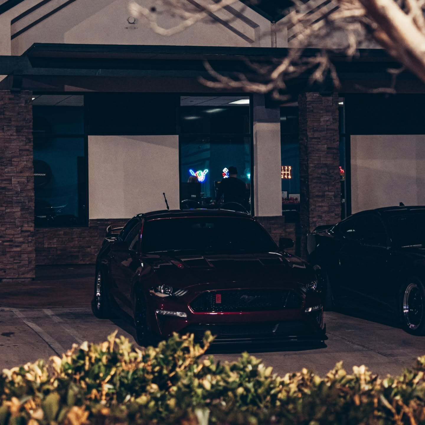 Dark sedan parked outside a storefront at night, with neon lights glowing inside the entrance.