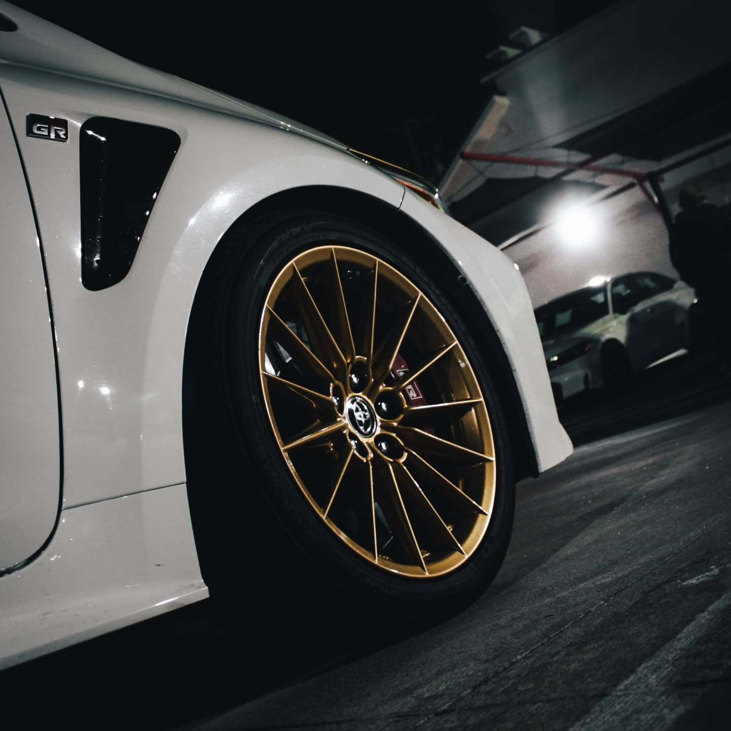 White sports car with gold wheels parked in a dark garage at night