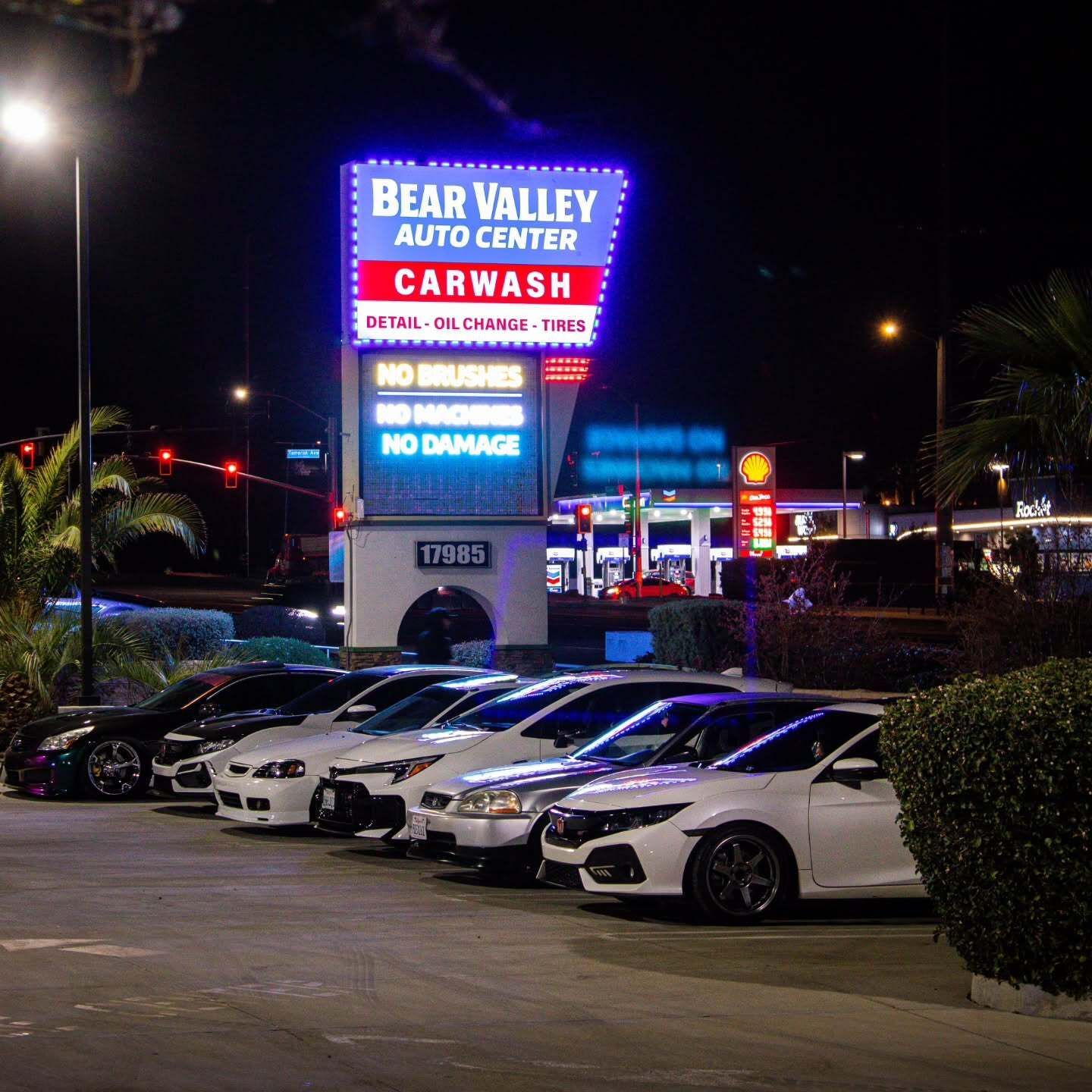 Nighttime car meet outside Bear Valley Auto Center Car Wash with rows of parked sports cars and bright neon signs