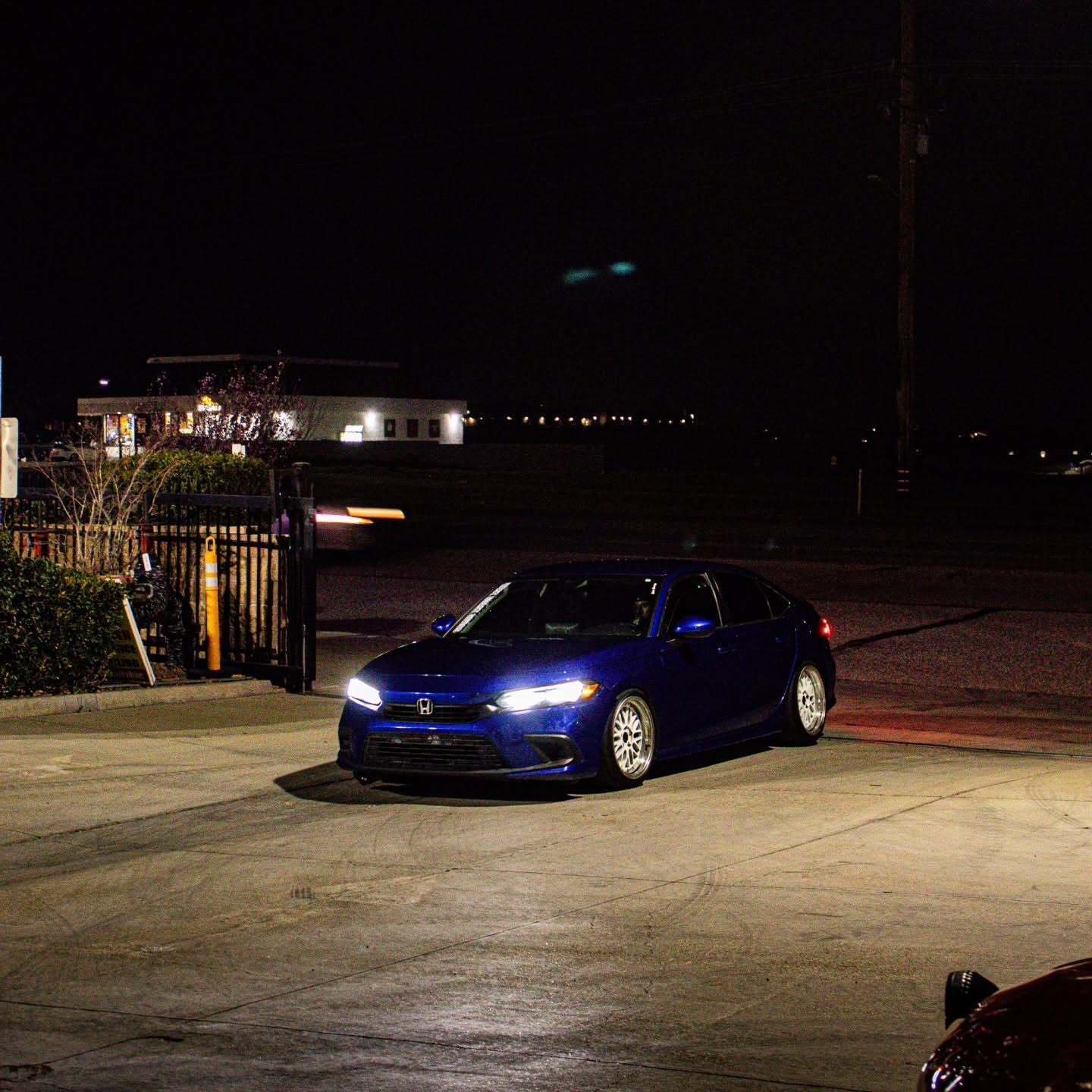 Blue sedan driving in a dimly lit parking lot at night