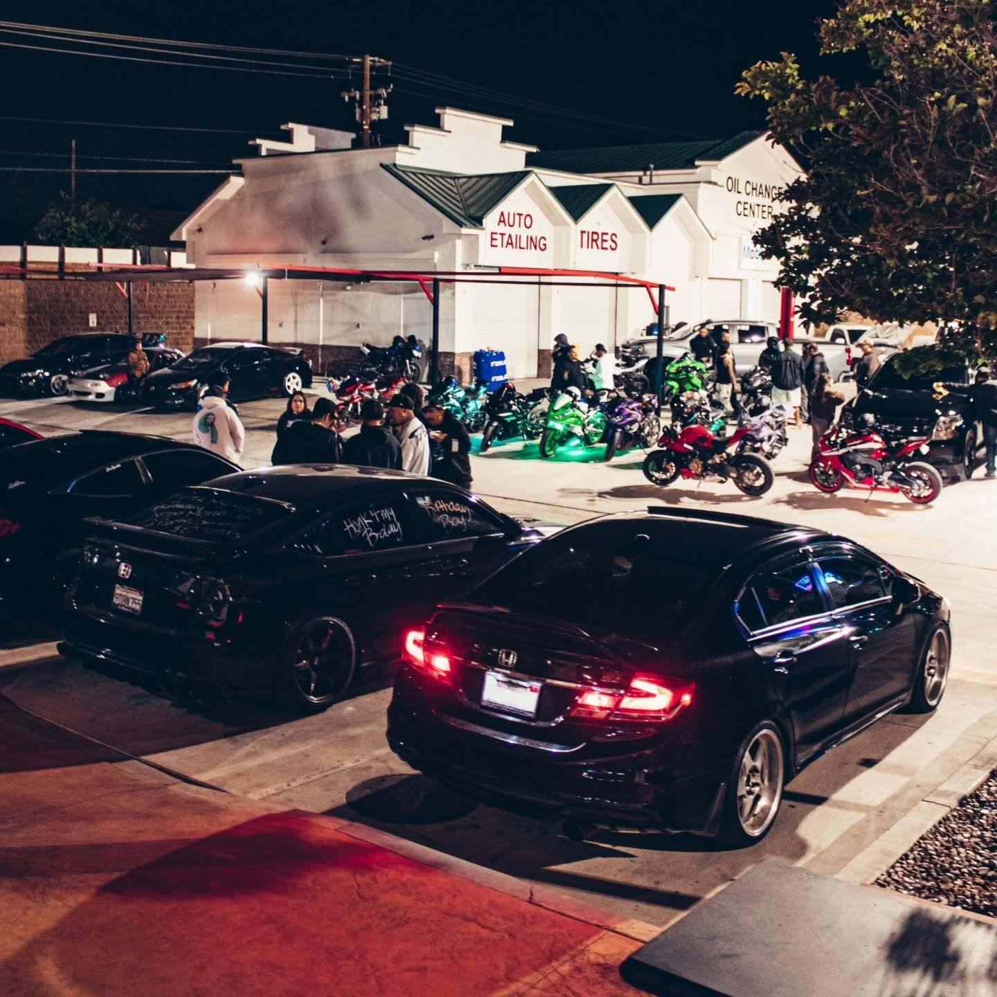 Night street meetup with black cars and motorcycles gathered outside a lit building