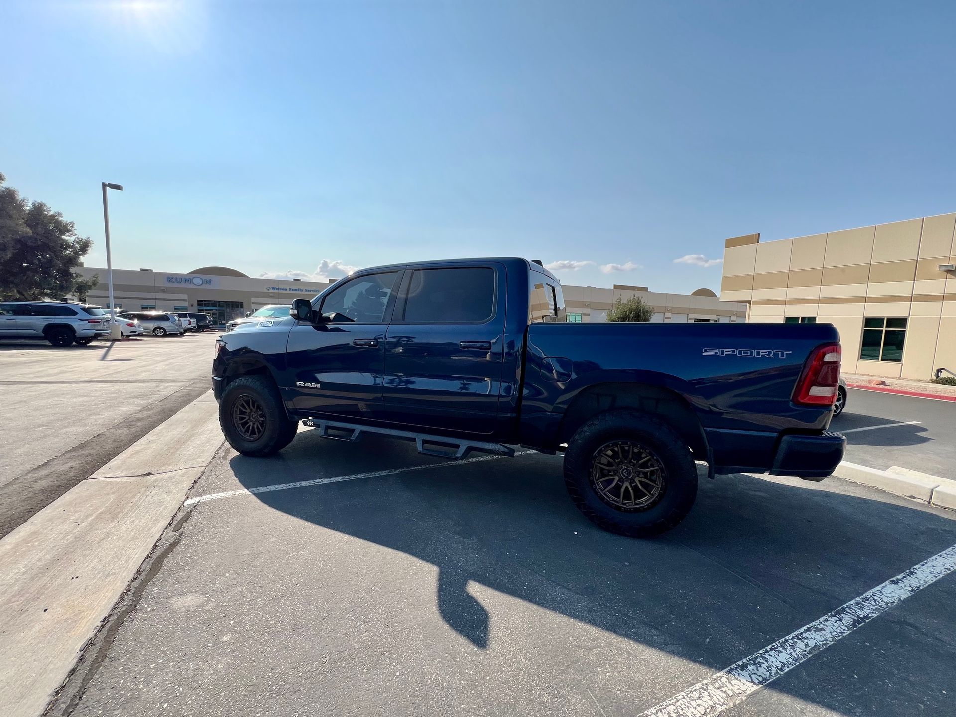 Blue pickup truck parked in a sunlit parking lot beside a beige building