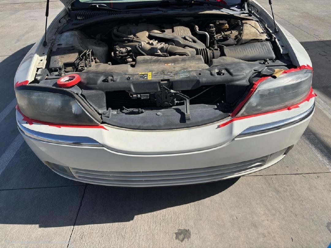 Rear of silver car with open hood, showing damaged engine compartment in a parking lot