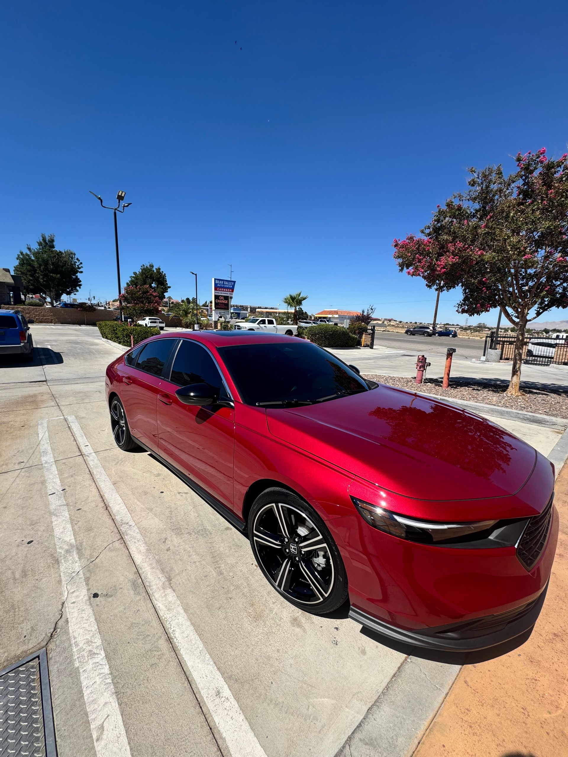 Red sedan parked in a sunny lot near the beach under a clear blue sky