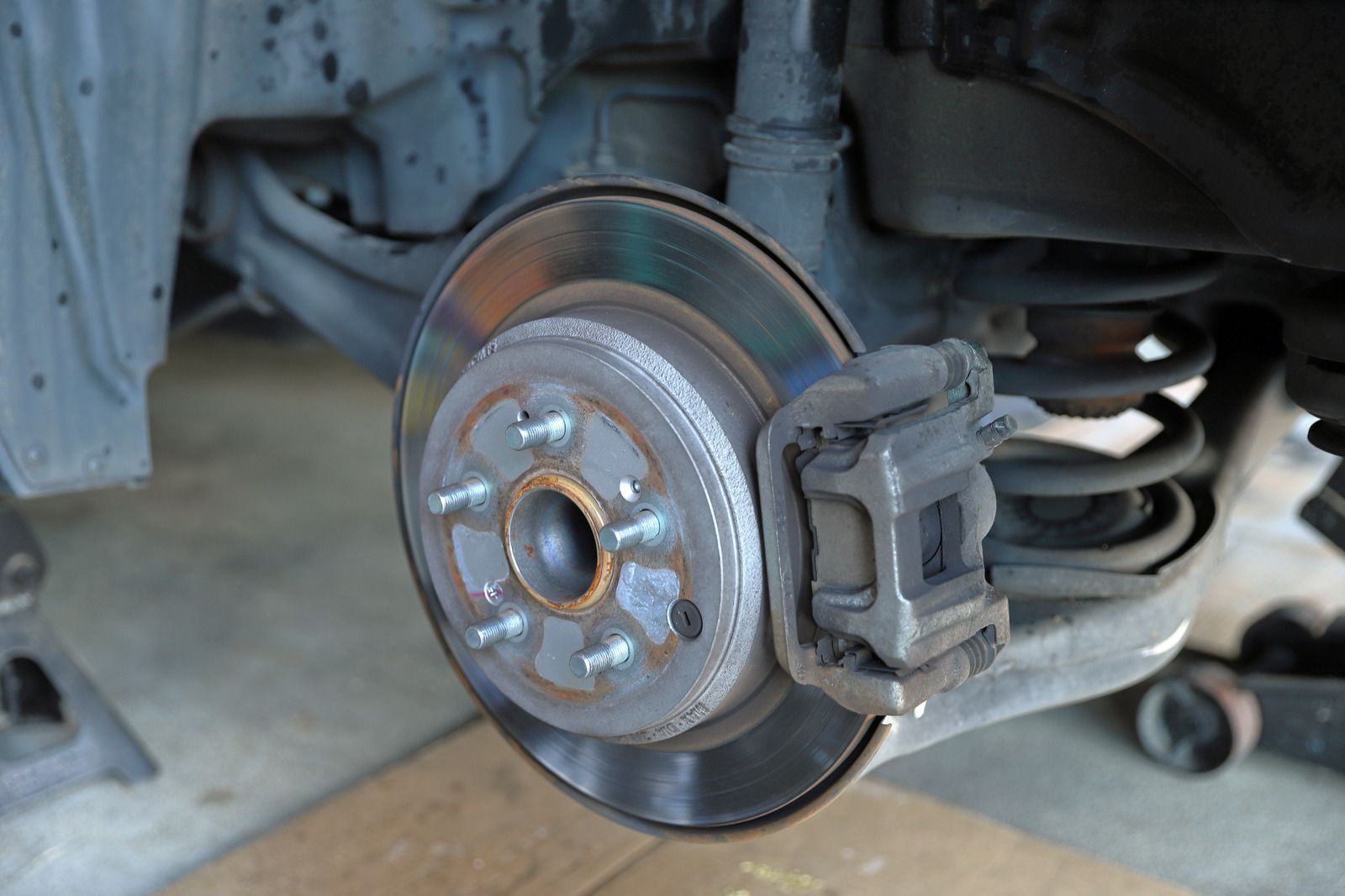 Car wheel hub with brake rotor and caliper exposed, parked on a concrete floor.