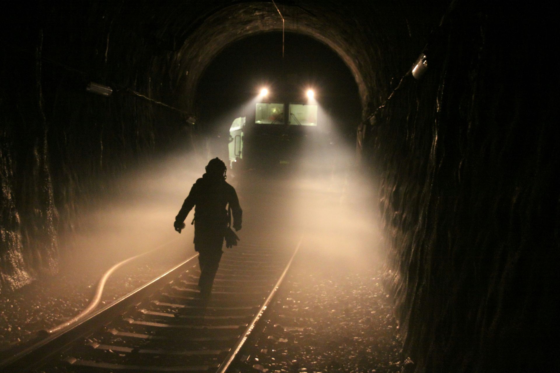 A silhouetted person walks in a dim tunnel toward a train ahead - fire emergency.