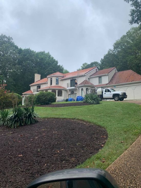 Large white house with red-tile roof, driveway, lawn, and cloudy sky