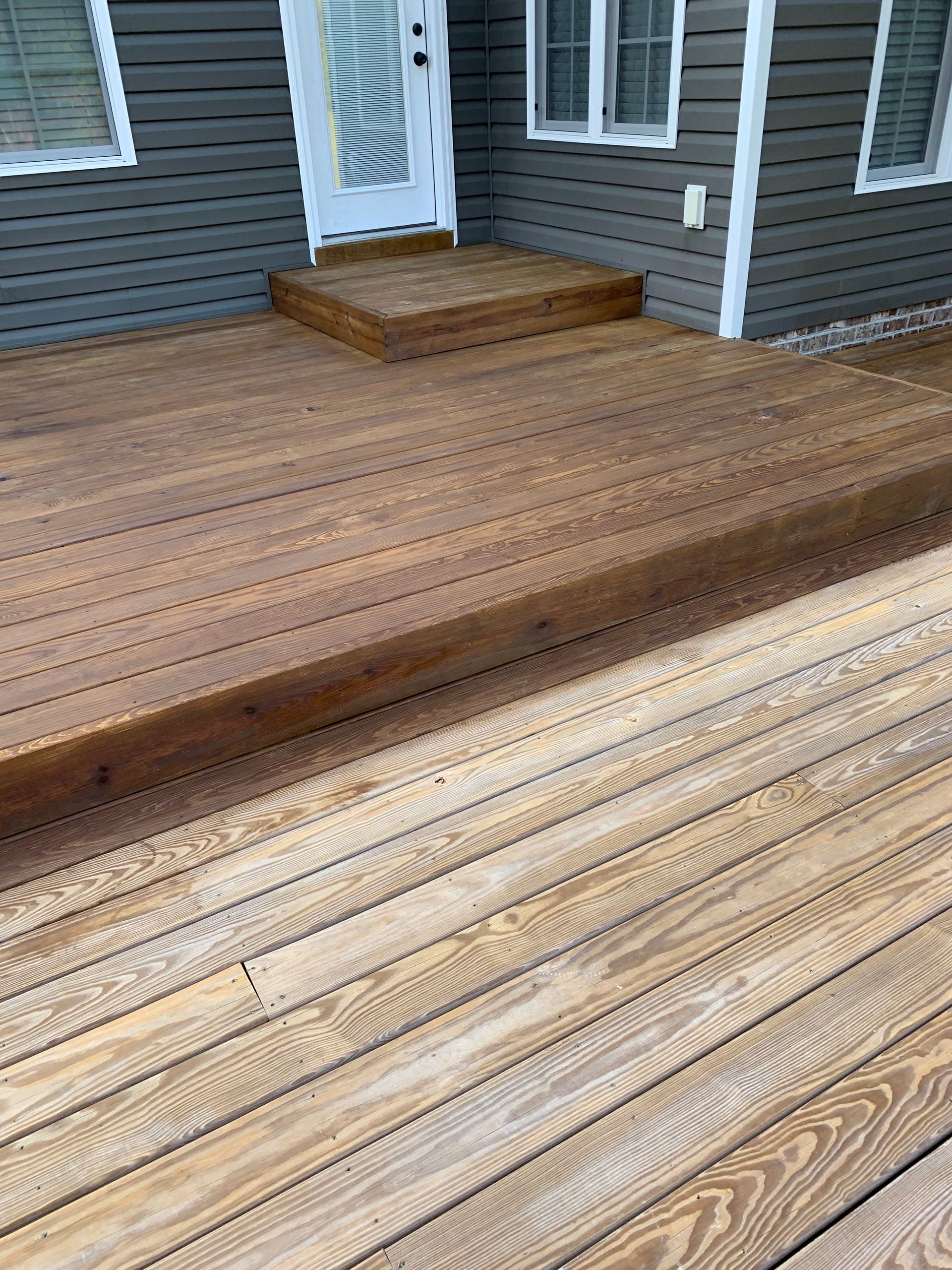 Wooden deck with gray house siding and a small step leading to a white door