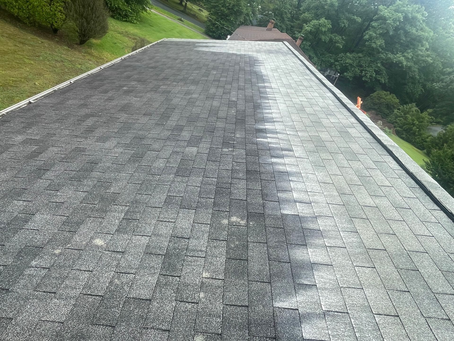 Gray shingled roof seen from above, with grassy slopes and trees on either side