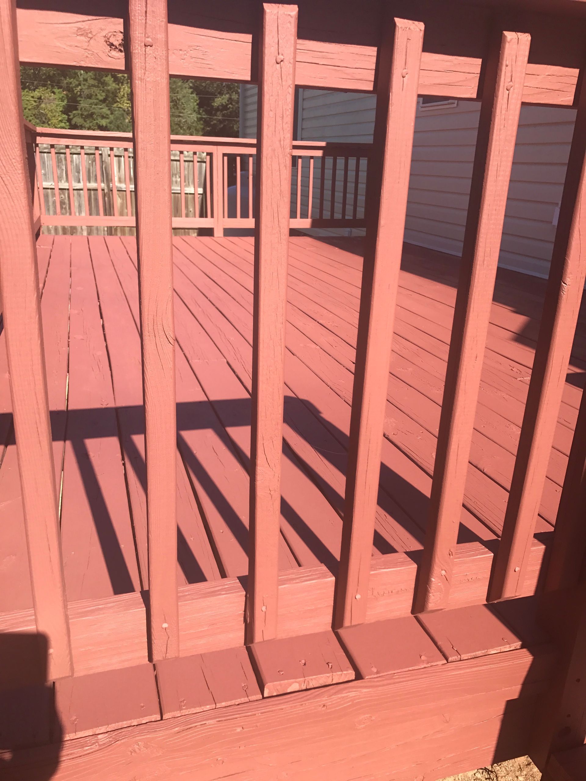 Pink wooden deck with vertical railings and stairs in sunlight