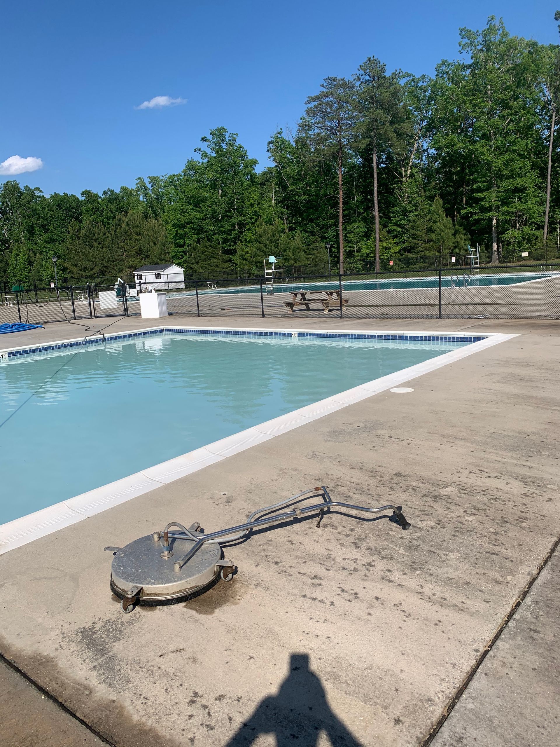 Empty outdoor swimming pool deck with a skimmer cover and trees in the background