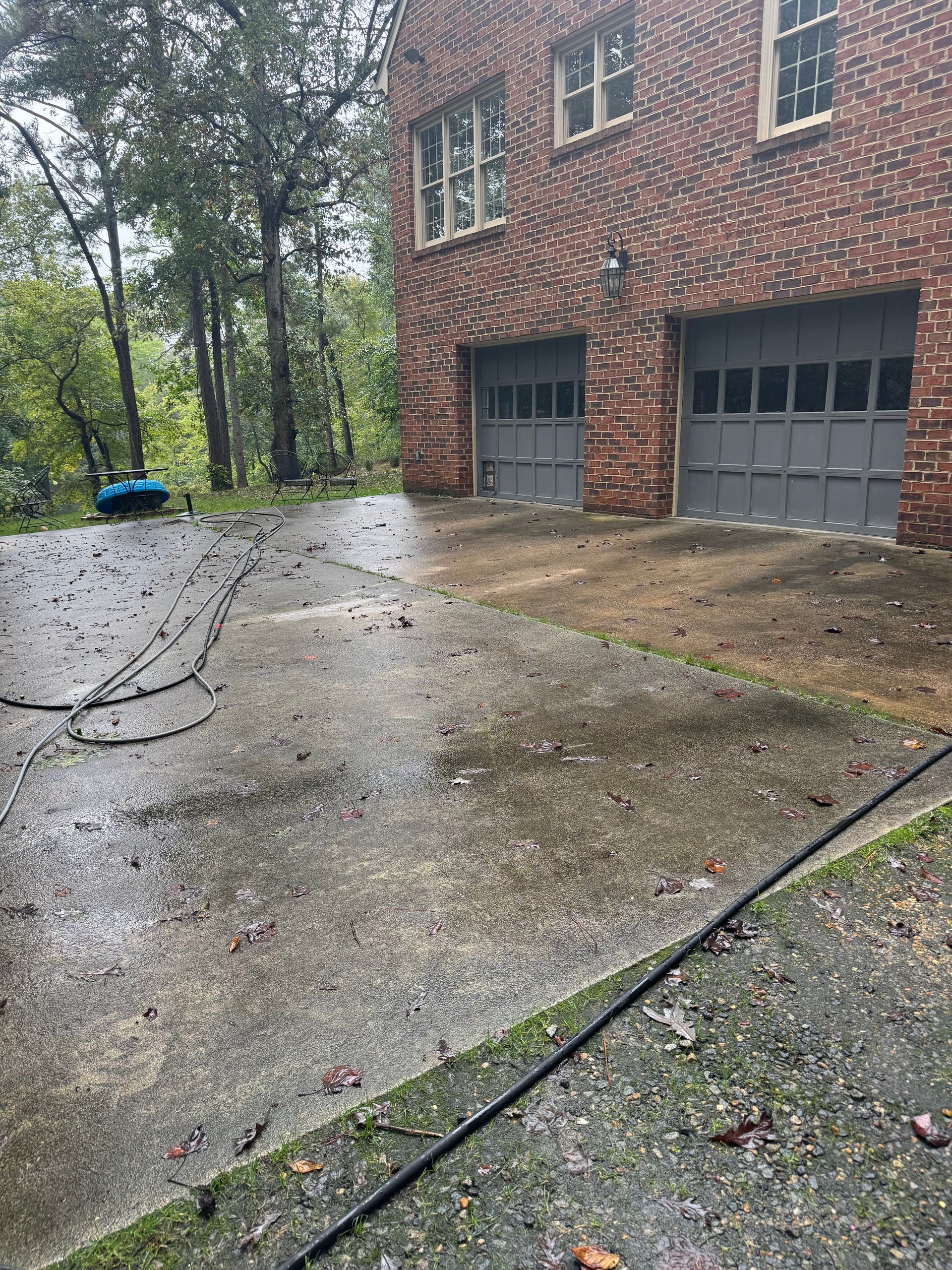 Brick house with two garage doors and a wet driveway covered in branches after a storm